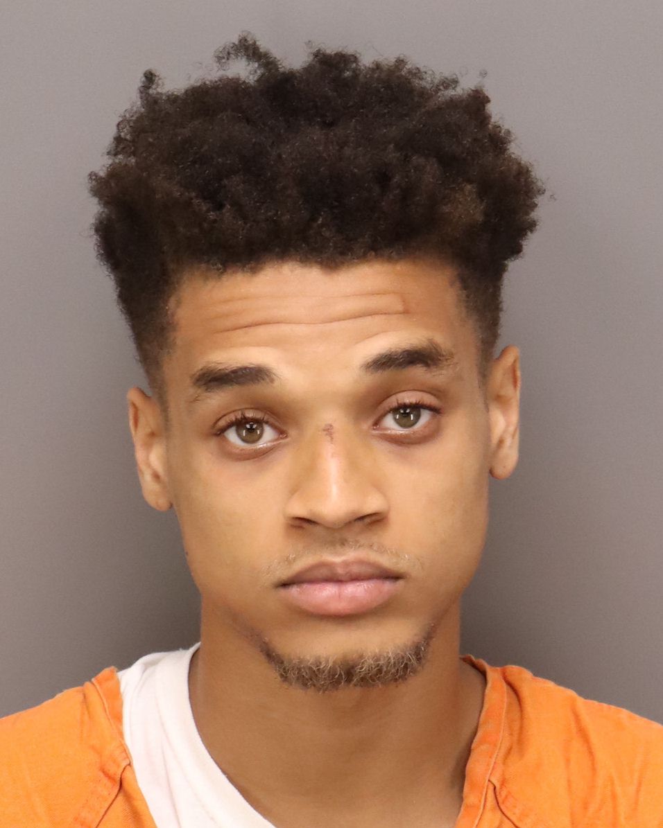 black man with brown eyes and tight brown coils wearing an orange shirt