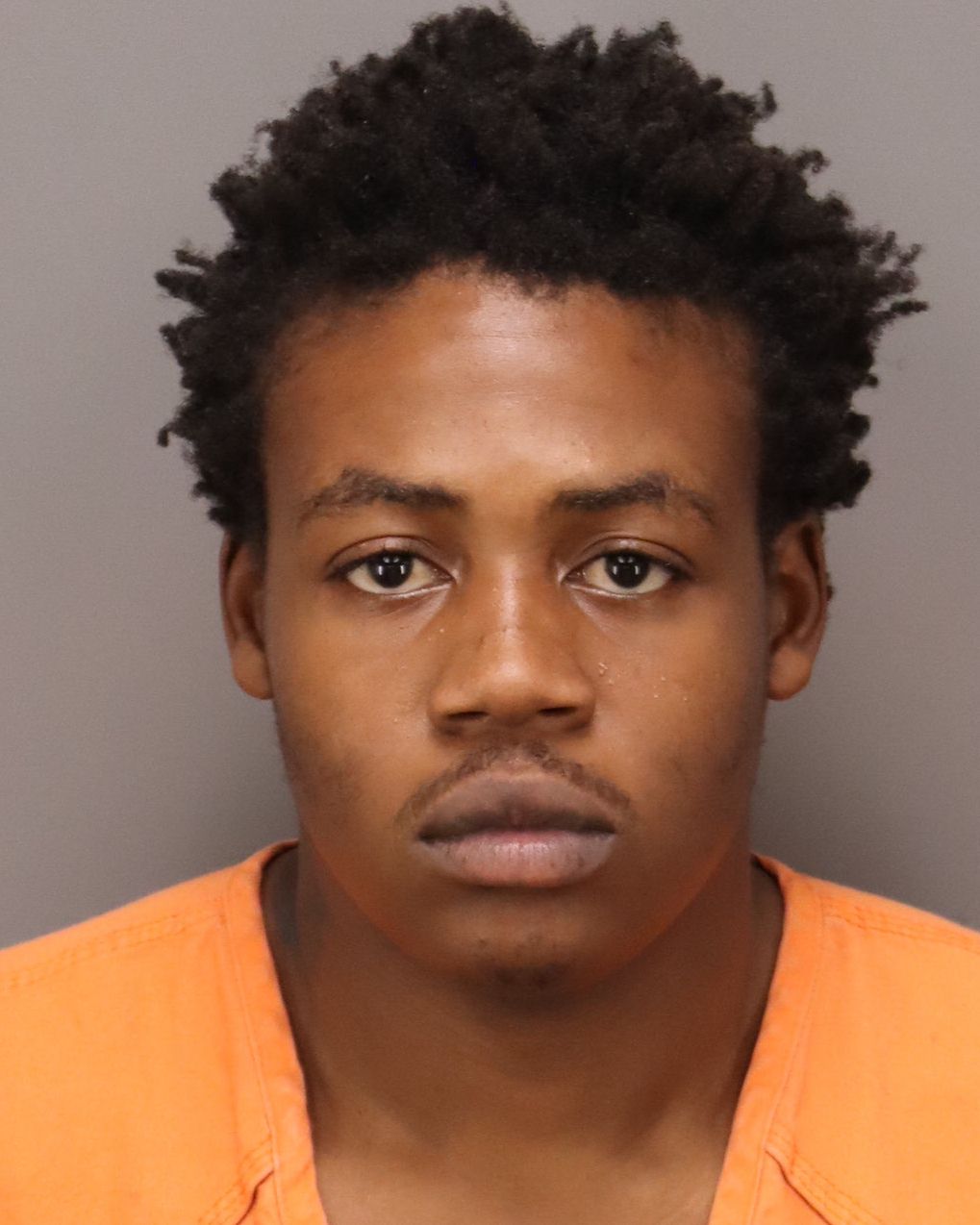 black man with short twisted short black hair wearing an orange shirt